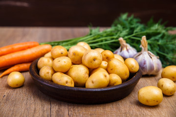 Potatoes in plate. Carrot, garlic and raw new potato. Fresh natural vegetables. Organic bio food on rustic wooden table.