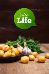 Potatoes in plate. Carrot tops, garlic and raw new potato. Fresh natural vegetables. Organic bio food on rustic wooden table.