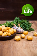 Potatoes in plate. Carrot tops, garlic and raw new potato. Fresh natural vegetables. Organic bio food on rustic wooden table.
