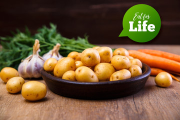 Potatoes in plate. Carrot, garlic and raw new potato. Fresh natural vegetables. Organic bio food on rustic wooden table.