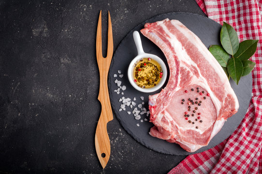 Raw meat with herbs, oil and spices on dark background. Raw pork steak. Ingredients for cooking meat. Top view. Copy space