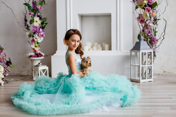 portrait of a beautiful young girl with blue eyes, with make up and hairstyle in a  lush turquoise dress with yorkshire terrier
