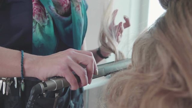 Close-up: a hairdresser makes curls from hair using a styler - a curling iron. Stylist. Beauty saloon. A stylist makes a haircut (curls) for a girl. Screwing the curls on the styler
