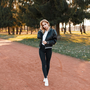 Beautiful woman in a black jacket, black jeans and white shoes in the park on a sunny day
