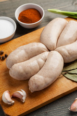 Raw chicken sausages for grille on a wooden board with spices ready for cooking, vertical