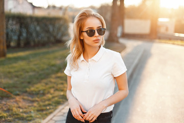 Young girl in trendy sunglasses and white polo shirt in a spring day at sunset