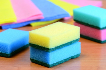 Obraz na płótnie Canvas Colorful sponge and rags for cleaning ware and house cleaning. Cleaning sponge with scrub and rags set on a wooden table. Closeup
