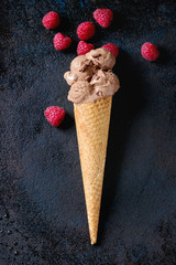 Chocolate ice cream mini balls in waffle cone with fresh raspberries over black metal texture background. Top view with space