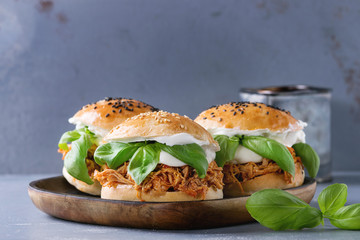 Homemade mini burgers with pulled chicken, basil, mozzarella cheese and yogurt sauce on wooden plate over gray texture background. Healthy fast food concept