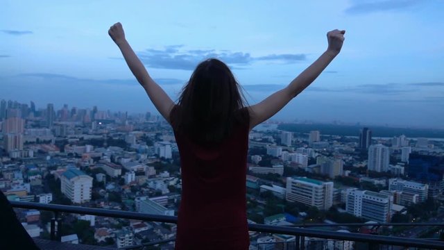 Successful, happy woman raising arms on terrace in the evening, super slow motion 240fps
