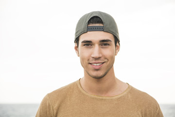 Portrait of handsome young man outside wearing baseball cap, looking at camera. Head and shoulders shot
