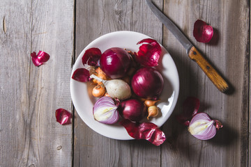 Several kinds of different onion bulbs at a white plate, standing on an old wooden table.