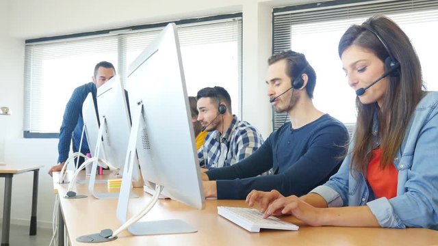 group of young people with desktop computer in row and headset training with teacher instructor in customer service call support helpline business center