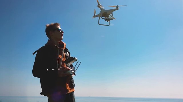 Quadrocopter drone takes off from the pilot's hand and hovers over the guy. The guy starts a drone on a green glade against the backdrop of the sea and cargo ships. Slow motion (120 fps).