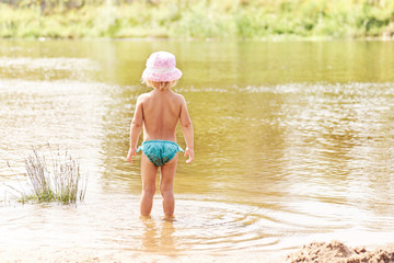 Little girl in swimsuit standing in the river during summer