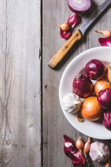 Several kinds of different onion bulbs at a white plate, standing on an old wooden table.