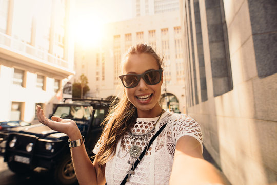 Tourist taking selfie in a street surrounded by buildings.