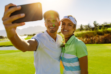 Smiling young couple taking selfie at golf course