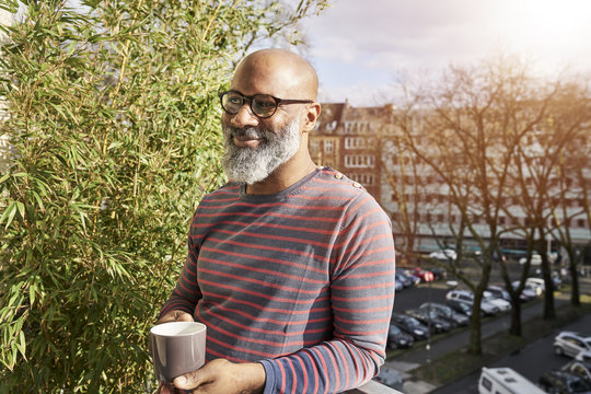 Mature man standing on balcony, drinking coffee