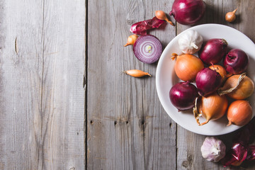 Several kinds of different onion bulbs at a white plate, standing on an old wooden table.