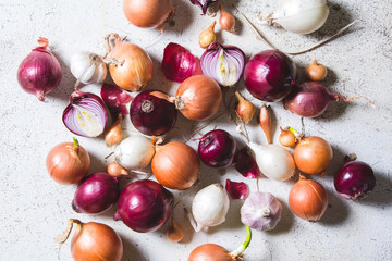 Several kinds of different onion bulbs lying on an old wooden table painted in white.