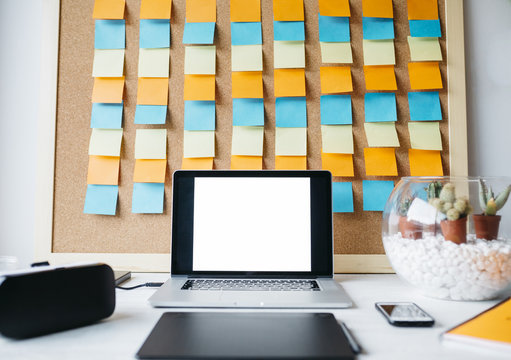 Desktop with laptop, virtual reality glasses, graphics tablet, cell phone, and notepads on pinboard