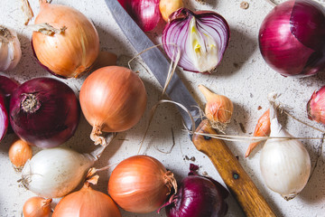 Several kinds of different onion bulbs lying on an old wooden table painted in white.