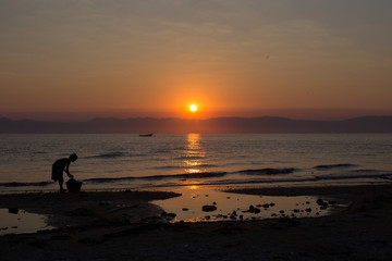 An African woman washes dishes on the shore of Lake Malawi at sunrise.