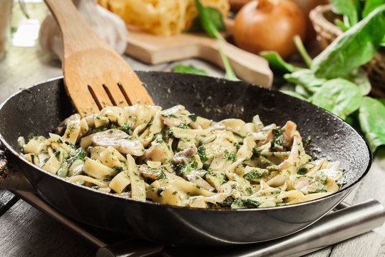 Tagliatelle pasta with spinach and mushrooms on a pan.