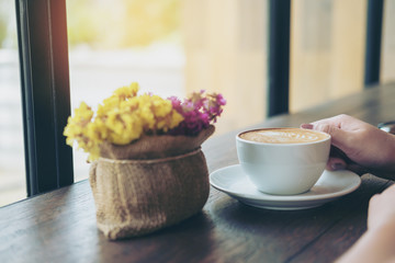Mockup image of a beautiful woman holding and showing white mobile phone with blank black screen with smiley face in vintage wooden cafe