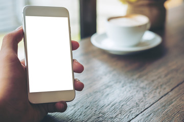 Mockup image of a beautiful woman holding and showing white mobile phone with blank black screen with smiley face in vintage wooden cafe