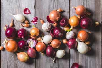 Several kinds of different onion bulbs lying on an old wooden table.