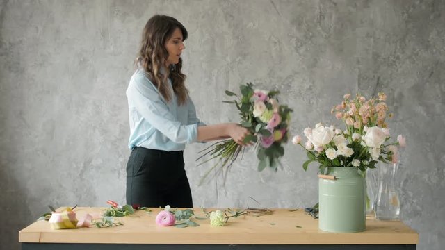 Florist at work: pretty young blond woman holds fashion modern bouquet of different flowers with peone and roses in craft paper