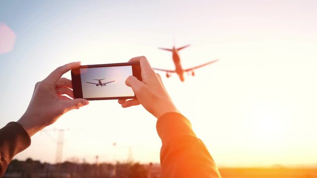 Cinemagraph of woman hands holding smart phone and taking video of big airplane landing in international airport hub at sunset time