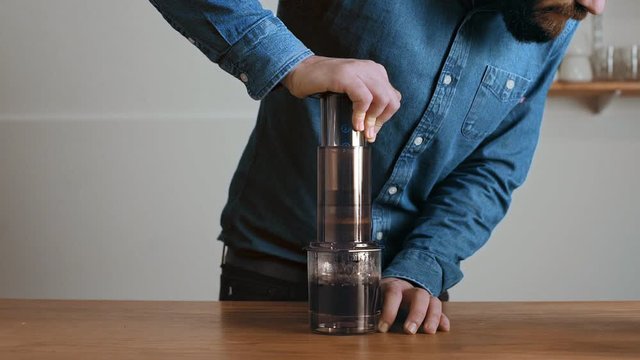 Cinemagraph loop of brutal bearded barista in blue jeans shirt makes aeropress to fill glass with beverage Professional alternative coffee brewing in artisan cafe shop