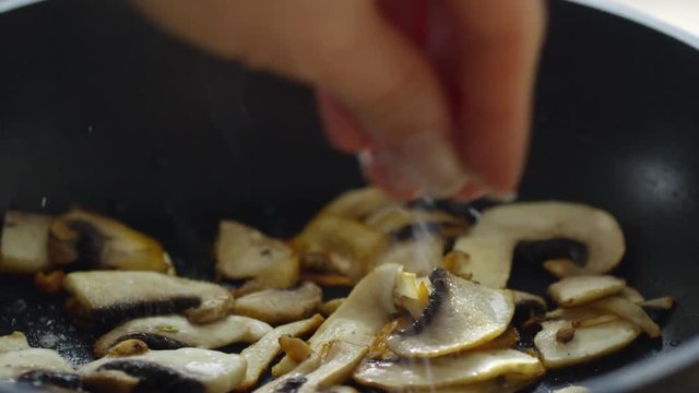 Closeup slow motion shot of hand adding salt to mushroom slices on frying pan