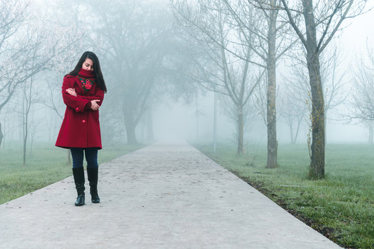 Young Woman In Red Walking By City Park In Fog