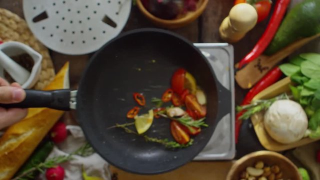 Top view of male hand holding frying pan and tossing up mixed vegetables in slow motion