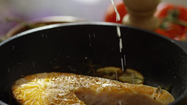 Tilt down of squeezing lemon juice on salmon steak while frying it on pan 