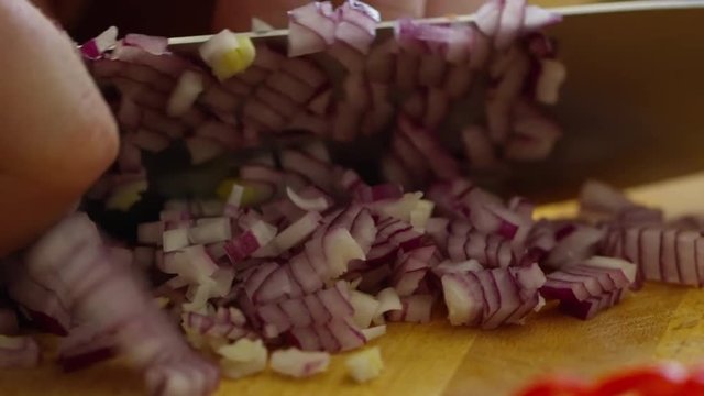 Closeup shot of chopping red onion with knife on wooden cutting board