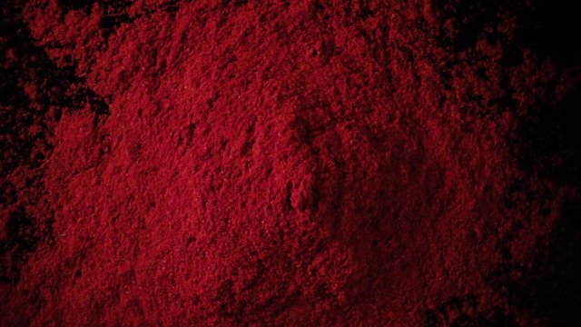 A large amount of paprika red powder drops down on the black table. Slow motion, top view