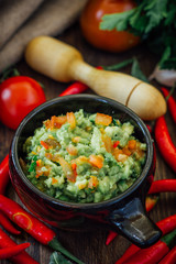 Guacamole dip with ingredietns in black ceramic bowl.