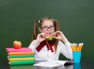 School girl eating sandwich near empty green chalkboard