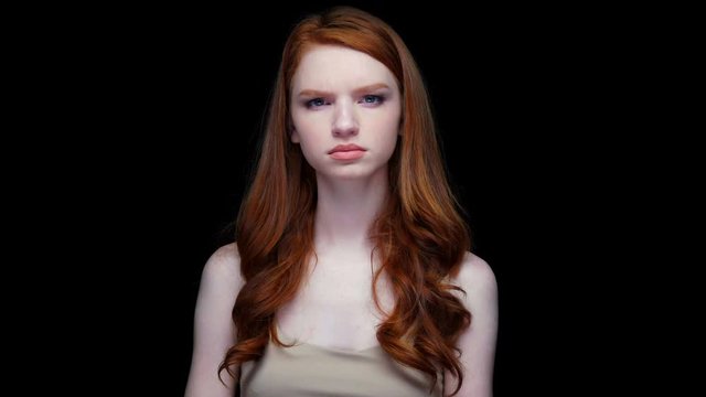 Unhappy dissatisfied young red haired woman looking at camera isolated over black 