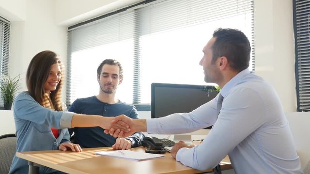 buying agreement contract signature and hand shaking between young couple and professional finance business man in office 