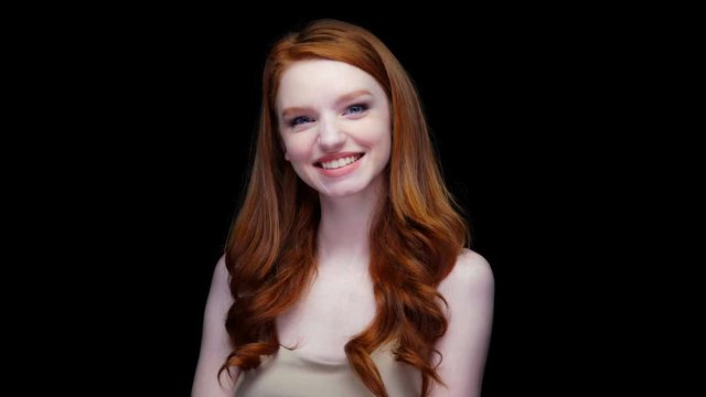 Smiling happy young red haired woman gesturing with hands in surprise gesture isolated over black 