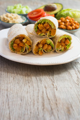 Vegetarian tortillas with chickpeas, butternut squash, spring onion, cucumber, avocado with ingredients on the back on the dark wooden table, copy space for text