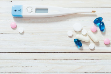  thermometer and pills from above on white wooden background