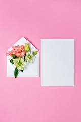 Colorful spring flowers in envelope and white sheet on pink background.