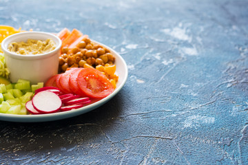 Rainbow colored vegetables, chickpeas on the white plae on the blue background, copy space for text